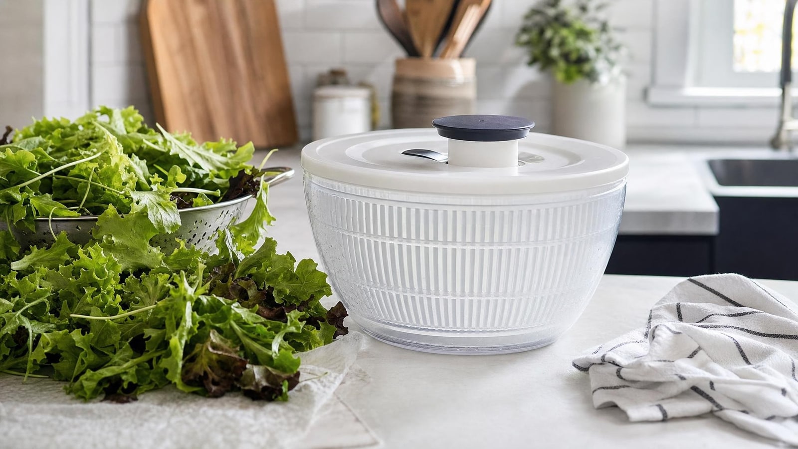 Fresh leafy greens beside a plain generic salad spinner and clean kitchen towel on a realistic home counter, no packaging or branding